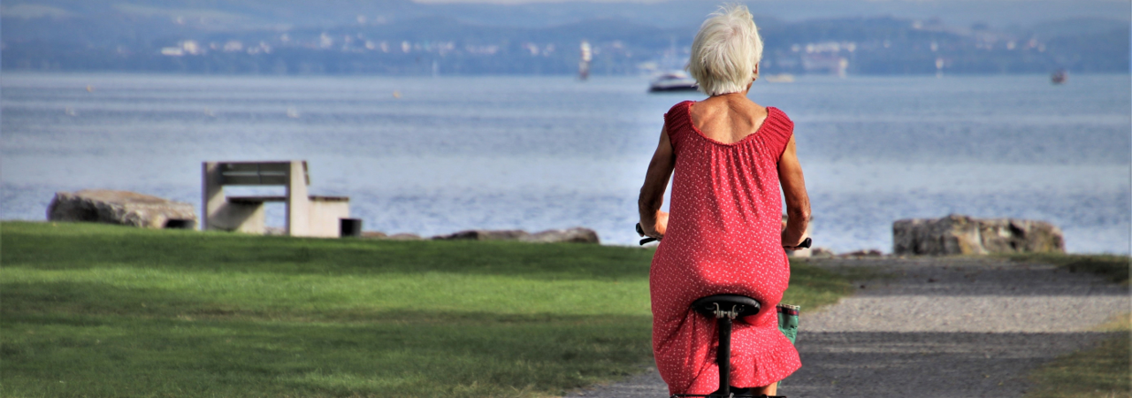 An elderly lady riding her bike near the sea front.